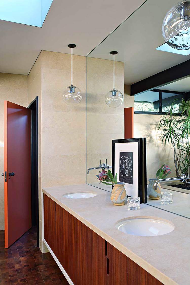 A primary bathroom in mid-century style featuring a double sink lighted by pendant lights.