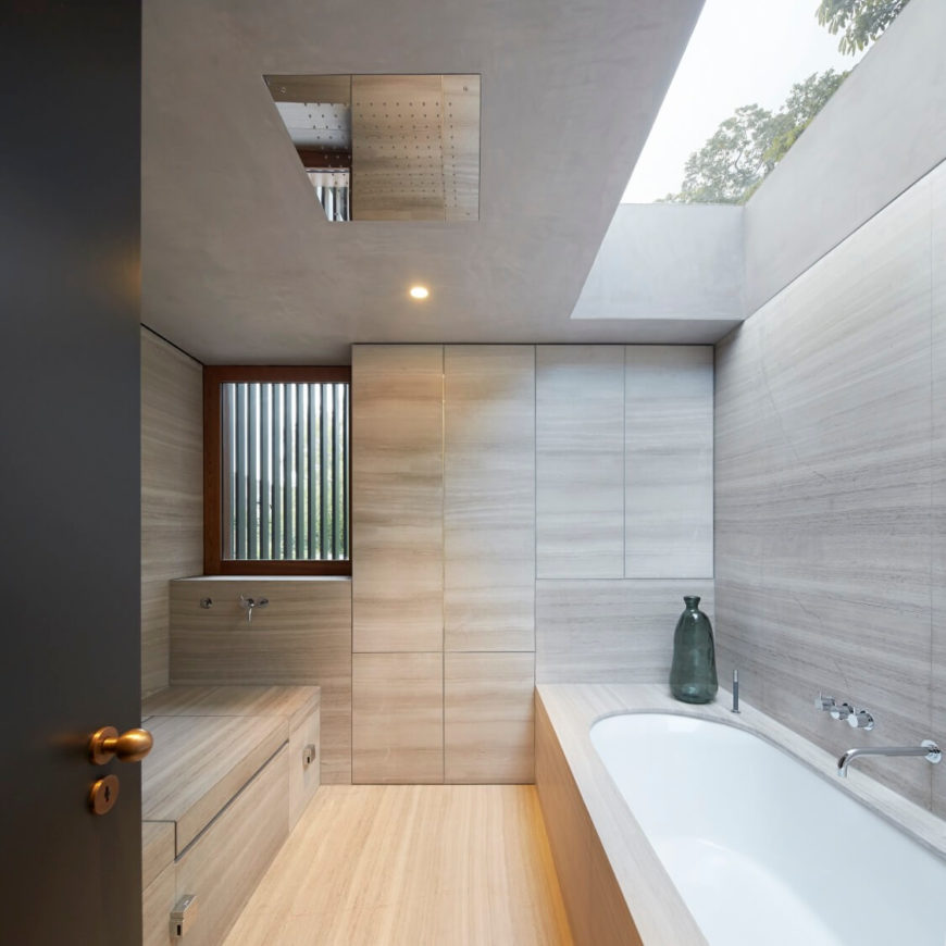 Cozy primary bathroom surrounded with light hardwood walls, flooring and built-in storage. Natural light streams through the skylight above the bathtub.