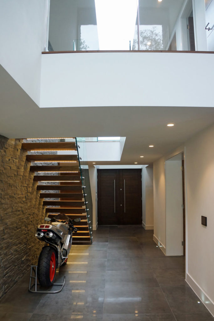 This hallway is illuminated with recessed lighting and strip lights from the floating staircase where a parked motorcycle is displayed.