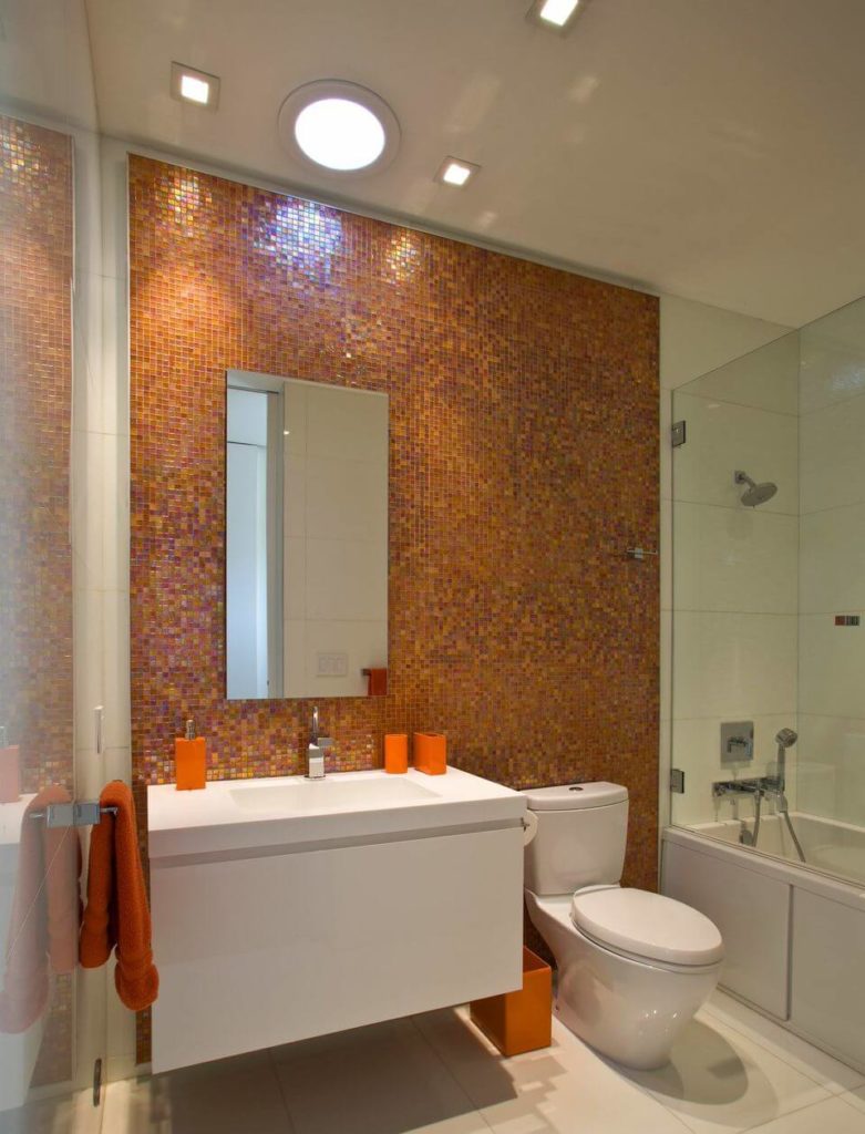 Charming primary bathroom with a burst of orange. It is accented with multi-colored glass mosaic tiles wall where a frameless mirror is mounted.