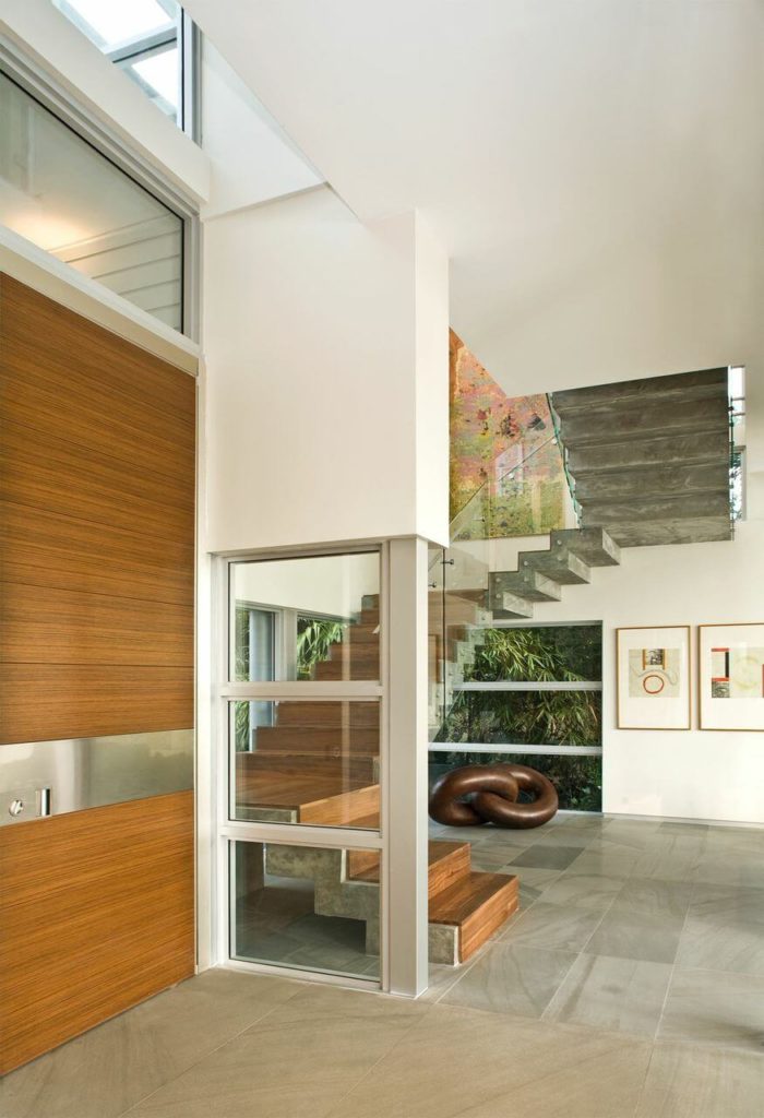 Contemporary foyer features a chain decor underneath the wooden staircase along with modern framed wall arts.