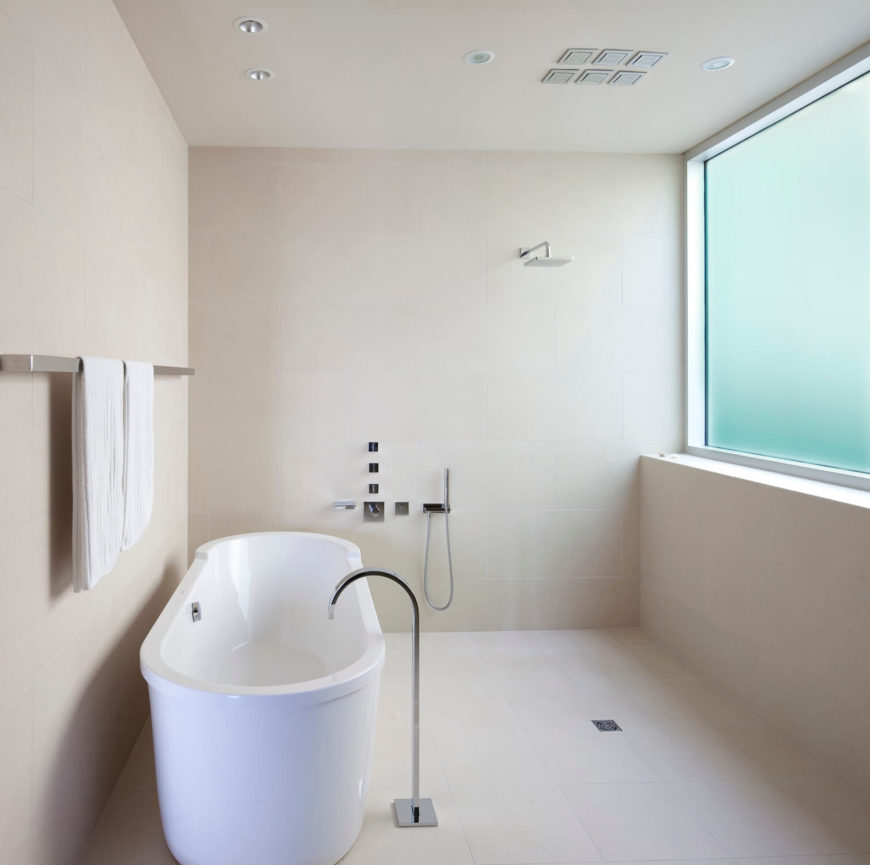 Primary bathroom with a pedestal tub and chrome fixtures. It is illuminated with recessed lighting along with natural lights coming through the frosted glass window.
