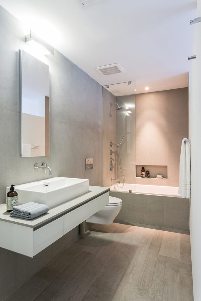 Sophisticated primary bathroom with a tub-shower combo illuminated by recessed lighting. It includes a white floating vessel sink vanity paired with a frameless vertical mirror.