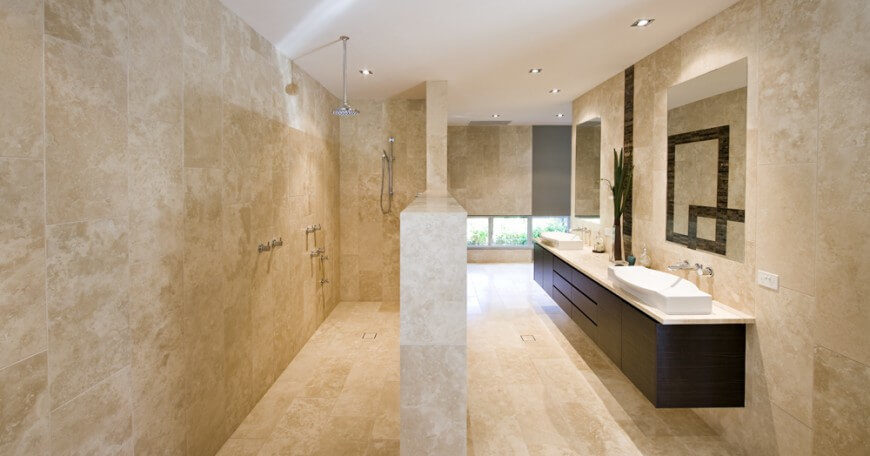 A half wall separates this large shower from the rest of the bathroom. The entire room is made of a light tan colored marble for a charming design. A half wall separates this large shower from the rest of the bathroom. The entire room is made of a light tan colored marble for a charming design.