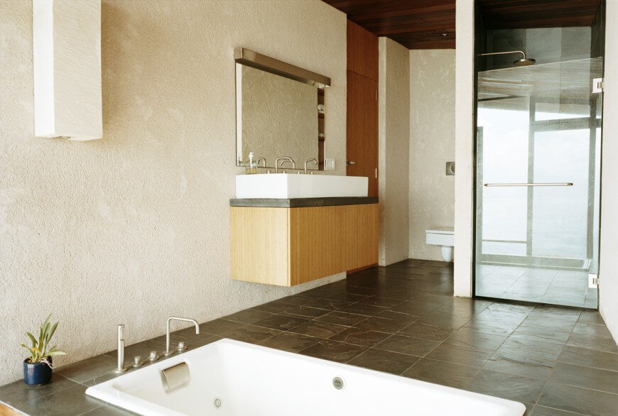This very unique bathroom has a bathtub built directly into the floor and a square toilet. The vanity and vessel sink are square and floating up from the ground. This very unique bathroom has a bathtub built directly into the floor and a square toilet. The vanity and vessel sink are square and floating up from the ground.