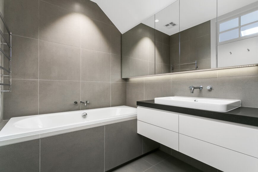 This minimalistic bathroom has a very calm and neutral color scheme. A large mirror move all the way across one wall and hovers over a floating vanity. This minimalistic bathroom has a very calm and neutral color scheme. A large mirror move all the way across one wall and hovers over a floating vanity.