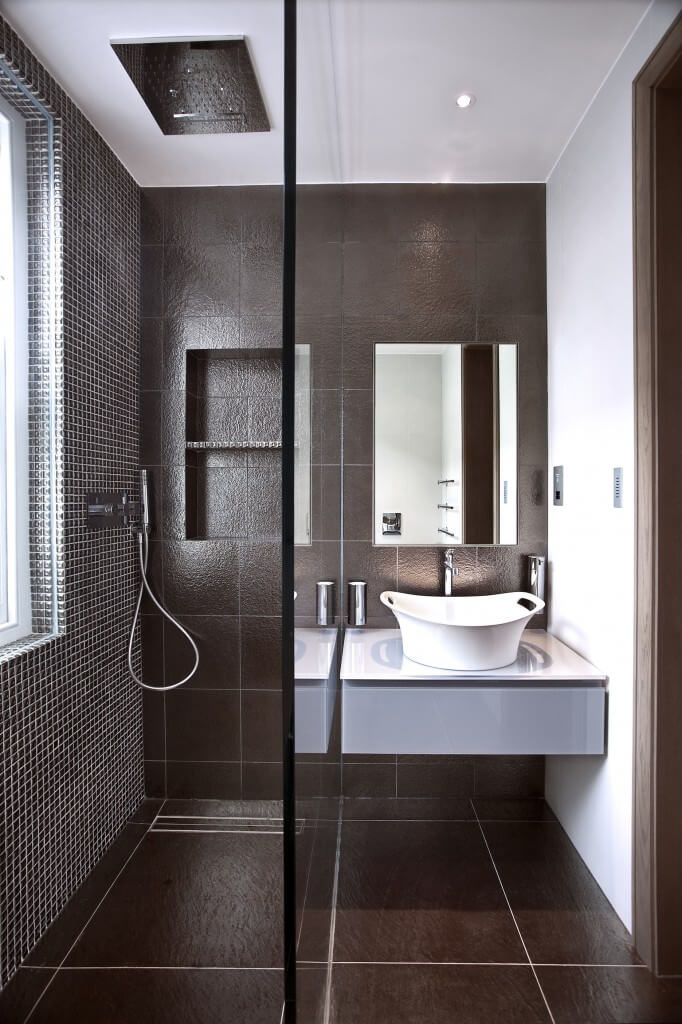 This elegant bathroom has a dark color scheme and a large glass enclosed shower. The vessel sink in this space is very unique and mimics a bucket. This elegant bathroom has a dark color scheme and a large glass enclosed shower. The vessel sink in this space is very unique and mimics a bucket.