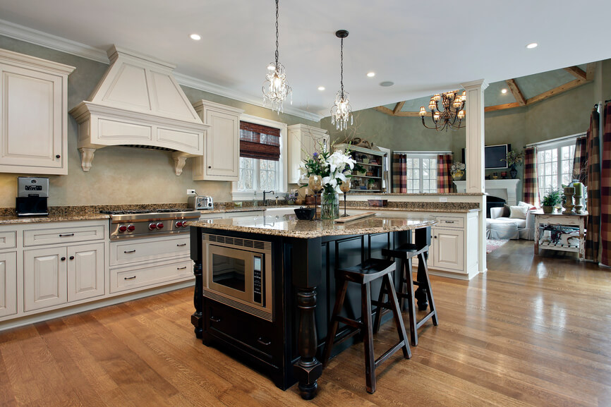 Within this sprawling, open-plan kitchen, the island stands in sharp contrast, flaunting a black stained wood construction and beige granite countertop. The island houses a stainless steel microwave, in addition to a curved expanse of countertop that provides ample dining space for a pair of wood bar stools. Within this sprawling, open-plan kitchen, the island stands in sharp contrast, flaunting a black stained wood construction and beige granite countertop. The island houses a stainless steel microwave, in addition to a curved expanse of countertop that provides ample dining space for a pair of wood bar stools.
