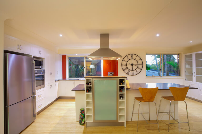This ultra-modern kitchen shrugs off the usual buttoned-down look of its contemporaries with flashes of bright color throughout. The island features an expansive dark countertop with dining space, plus a tall wine rack and cooled storage rising above. This extra feature backs up a built-in range, with stainless steel hood vent overhead. This ultra-modern kitchen shrugs off the usual buttoned-down look of its contemporaries with flashes of bright color throughout. The island features an expansive dark countertop with dining space, plus a tall wine rack and cooled storage rising above. This extra feature backs up a built-in range, with stainless steel hood vent overhead.