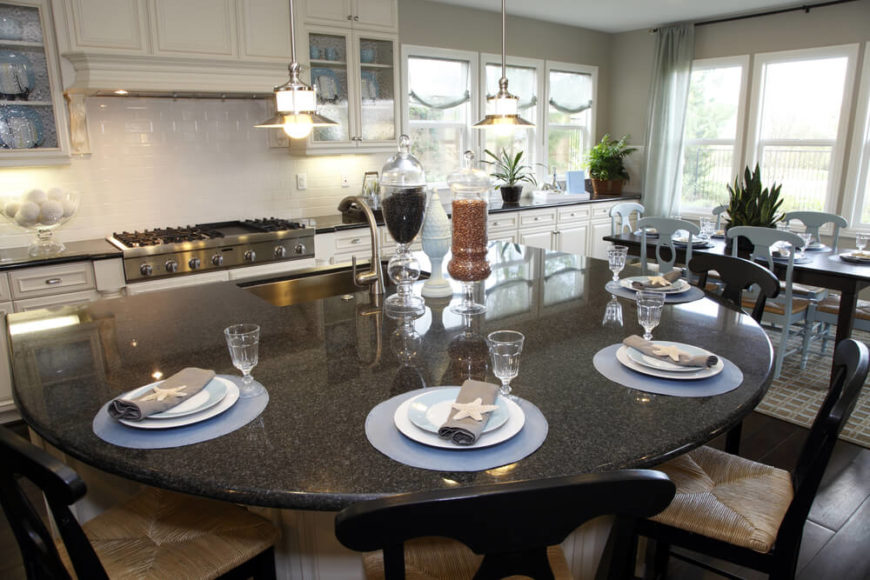Here we see another sprawling open-design kitchen, this time in pristine whites over a dark hardwood floor. The island is a massive semi-circle design, with large basin sink on the flat end and a large curved space for in-kitchen dining. Dark granite countertop adds to the bold contrast in this brightly sunlit room. Here we see another sprawling open-design kitchen, this time in pristine whites over a dark hardwood floor. The island is a massive semi-circle design, with large basin sink on the flat end and a large curved space for in-kitchen dining. Dark granite countertop adds to the bold contrast in this brightly sunlit room.