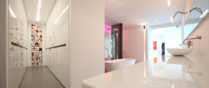 An angled view of the primary bathroom showcasing the color-changing neon lights in the shower area and a glass top counter with vessel sinks.