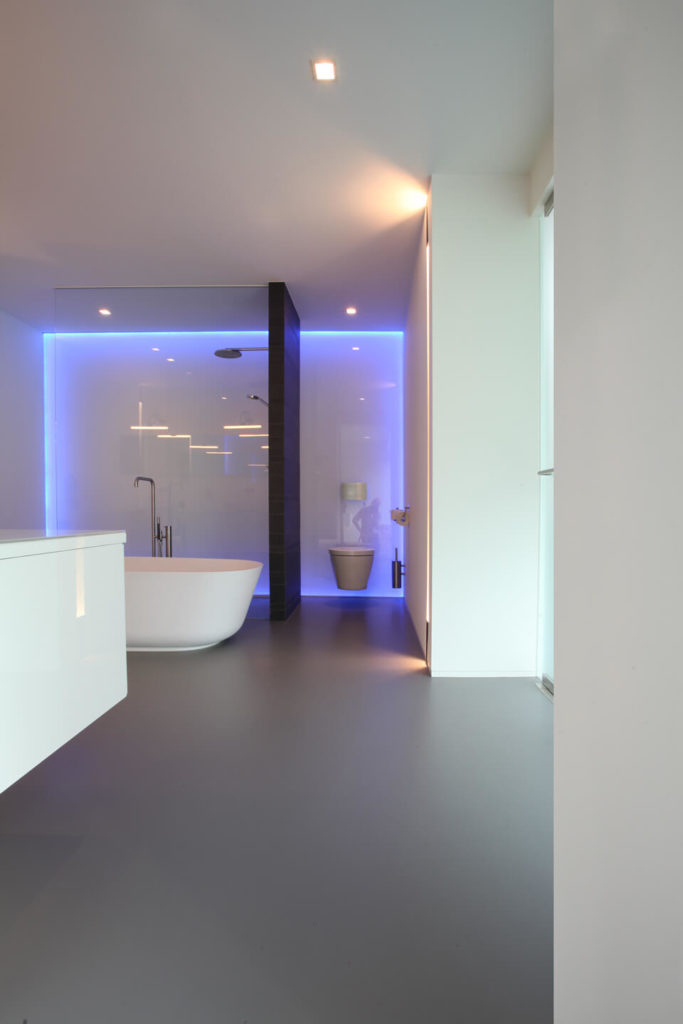 Gorgeous primary bathroom features a walk-in shower and toilet area accented with neon lights and divided by a dark wood plank wall.