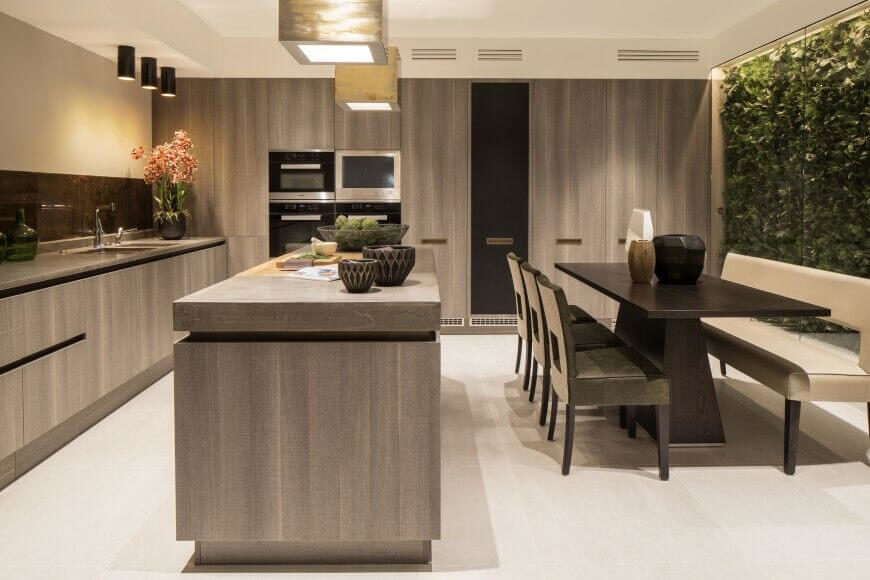 Gray wood is the main component of this luxurious kitchen, which features floor-to-ceiling windows on the right behind the dining set. Slim black appliances are inset into the minimalist cabinetry. Gray wood is the main component of this luxurious kitchen, which features floor-to-ceiling windows on the right behind the dining set. Slim black appliances are inset into the minimalist cabinetry.