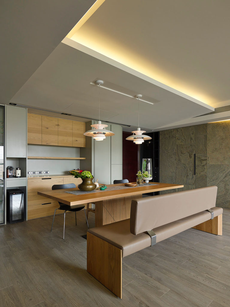 Cozy dining room with a rectangular wood table paired with a tufted bench and black chairs. It is illuminated by a pair of pendant lights that hung from the suspended ceiling.