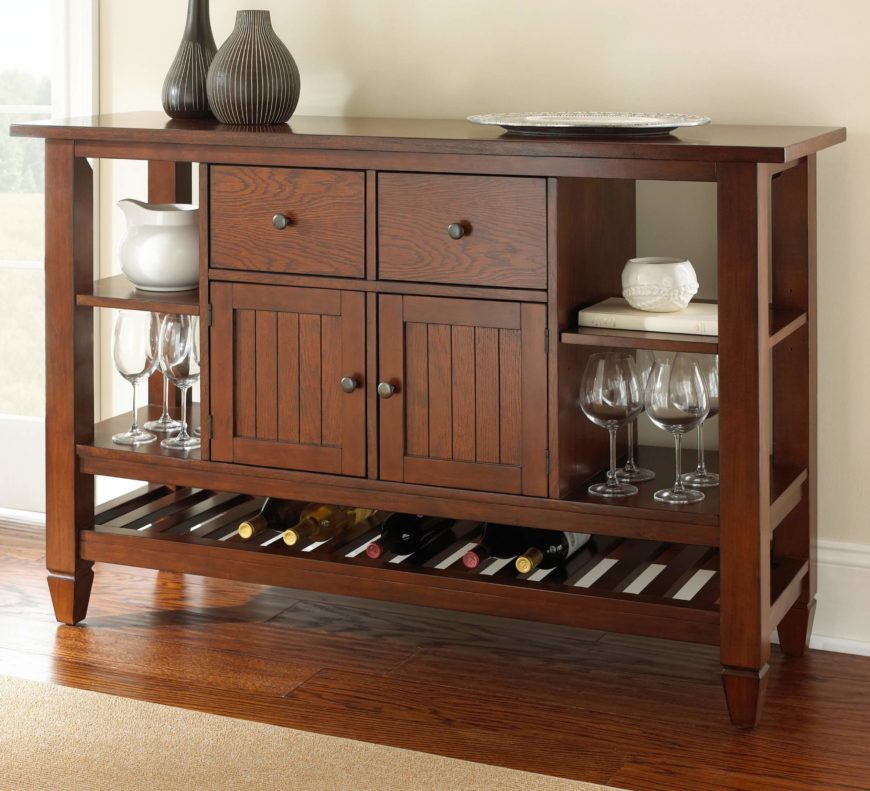 The bottom of this serving table includes a large wine rack. Glasses are stored on either side of the cabinets, with drawers above. The bottom of this serving table includes a large wine rack. Glasses are stored on either side of the cabinets, with drawers above.