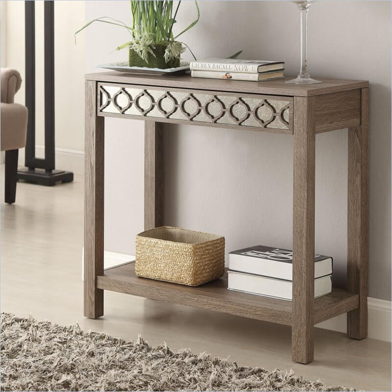 A reflective surface beneath the repeating pattern on the front draws the eye to this table, which has a prominent wood grain and a silvery color. A reflective surface beneath the repeating pattern on the front draws the eye to this table, which has a prominent wood grain and a silvery color.