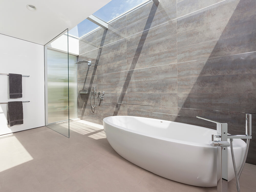 Minimalist primary bathroom showcases a large freestanding bathtub along with a walk-in shower that includes a glass divider and skylight which spans the length of the room.