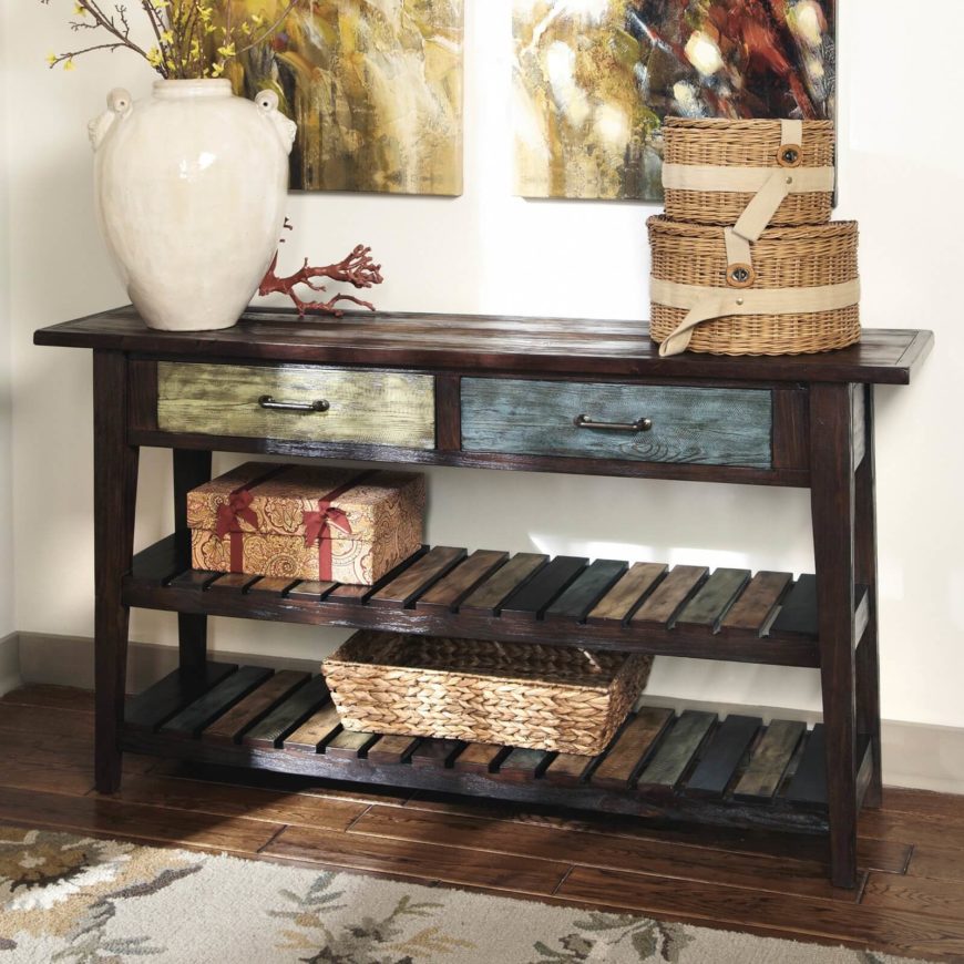 The drawers of this lightly distressed table are painted light green and light blue, contrasting with the dark, natural wood of the rest of the table. The two lower shelves are covered in multi-colored slats. The drawers of this lightly distressed table are painted light green and light blue, contrasting with the dark, natural wood of the rest of the table. The two lower shelves are covered in multi-colored slats.