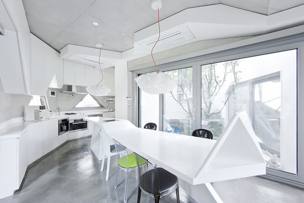 White dining room features a lengthy modern dining table that extends with the breakfast island accented by multi-colored chairs over concrete flooring.