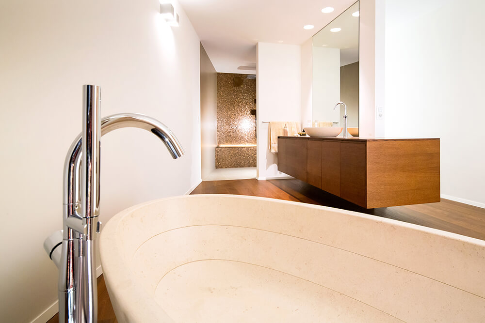Spacious primary bathroom features a granite pedestal tub and floating wooden vanity with a vessel sink along with a walk-in shower from afar.