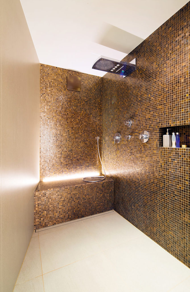 Fabulous walk-in shower area with brown mosaic tiles accented with a modern shower head and chrome fixtures.