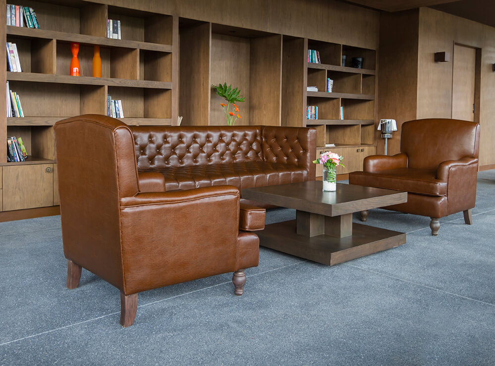 A home library featuring large tiles flooring and brown leather seats with a stylish center table.