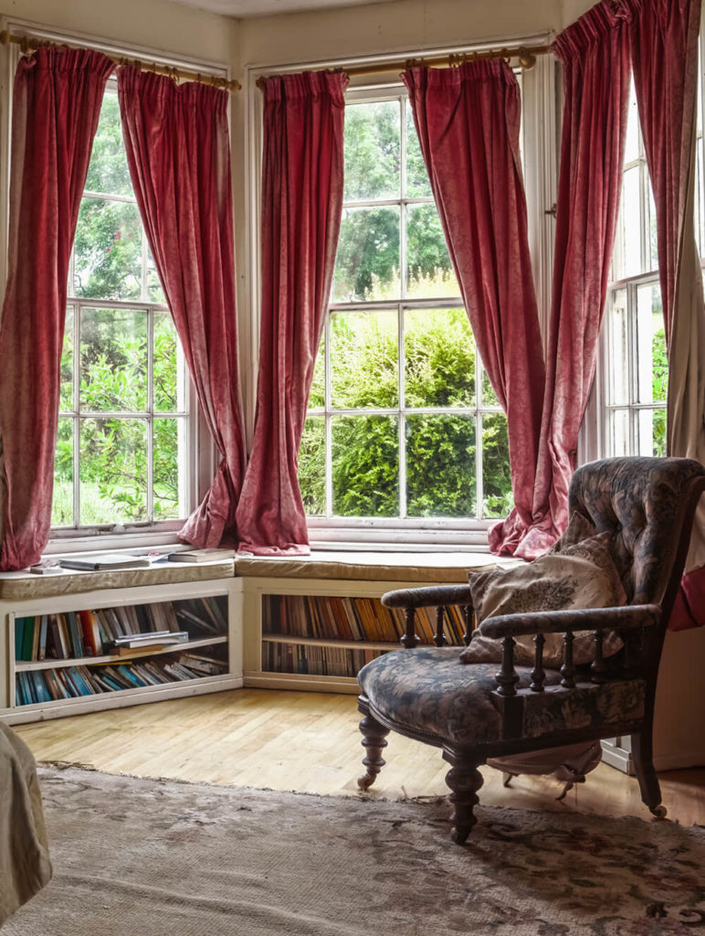 This home library boasts French windows overlooking the pretty outdoor views. The windows offer red window curtains.