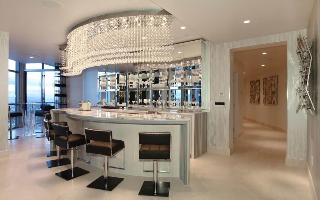 Large bar featuring a stunning bar counter paired by black stylish bar stools lighted by a glamorous set of ceiling lighting.