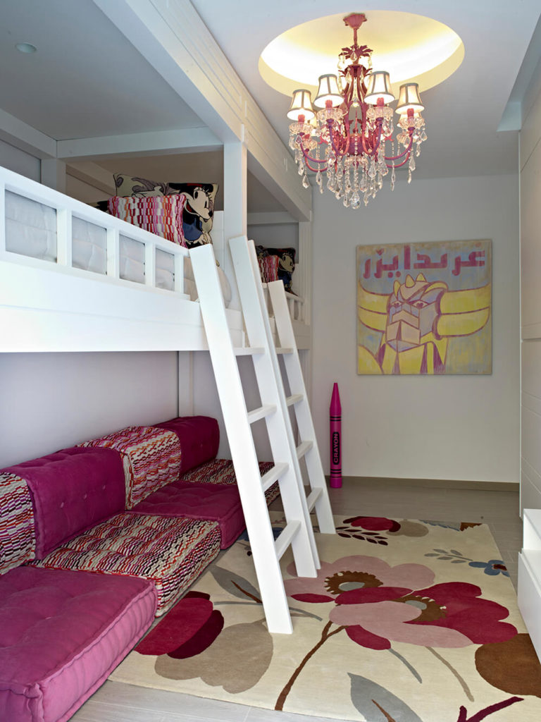 Small girl's bedroom with elegant bed and seats. The rug and wall decors look very lovely as well as the glamorous chandelier.
