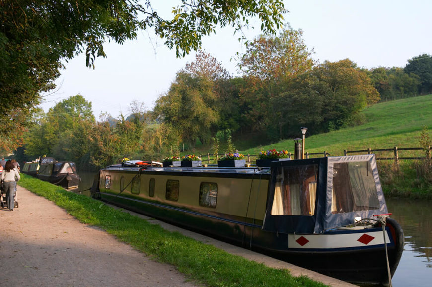 A lengthy houseboat with displays of flowers along the top. This houseboat is moored along a canal in the Netherlands, across from a beautiful meadow. A lengthy houseboat with displays of flowers along the top. This houseboat is moored along a canal in the Netherlands, across from a beautiful meadow.