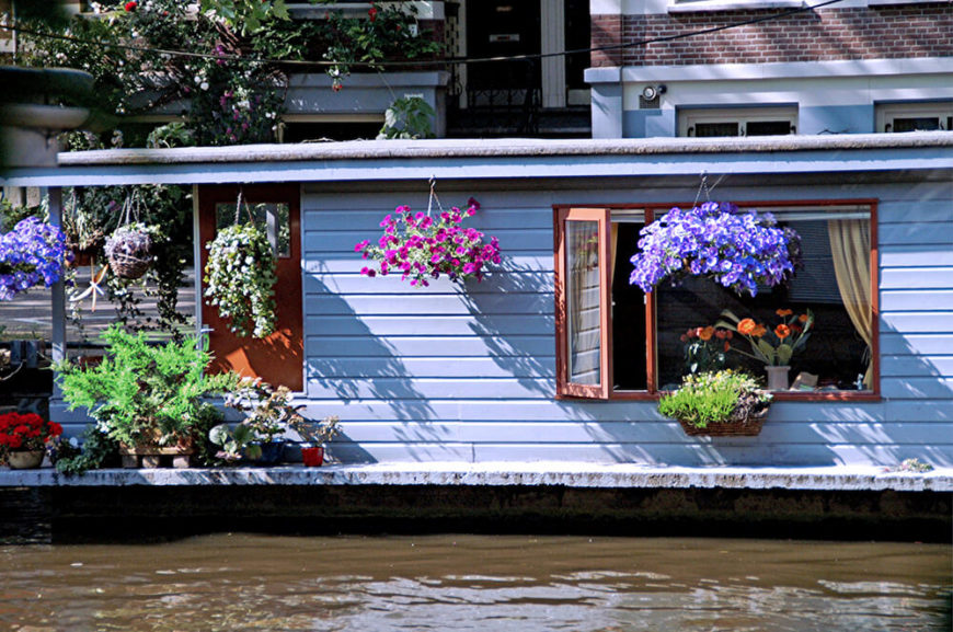 A single story houseboat with a wealth of colorful hanging baskets, window boxes, and containers of plants all along the porch. A single story houseboat with a wealth of colorful hanging baskets, window boxes, and containers of plants all along the porch.