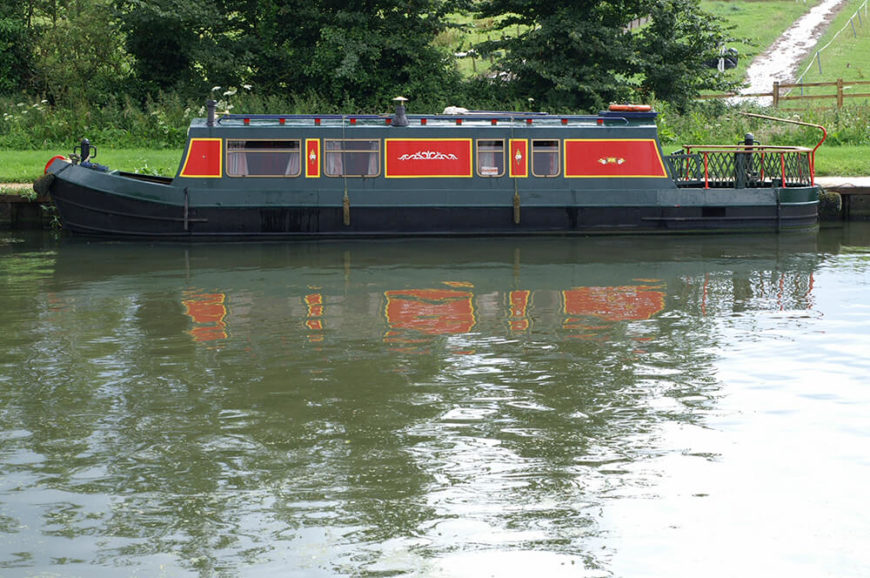 A large mobile houseboat in the Netherlands in a deep forest green with bold red and yellow panels. A large mobile houseboat in the Netherlands in a deep forest green with bold red and yellow panels.
