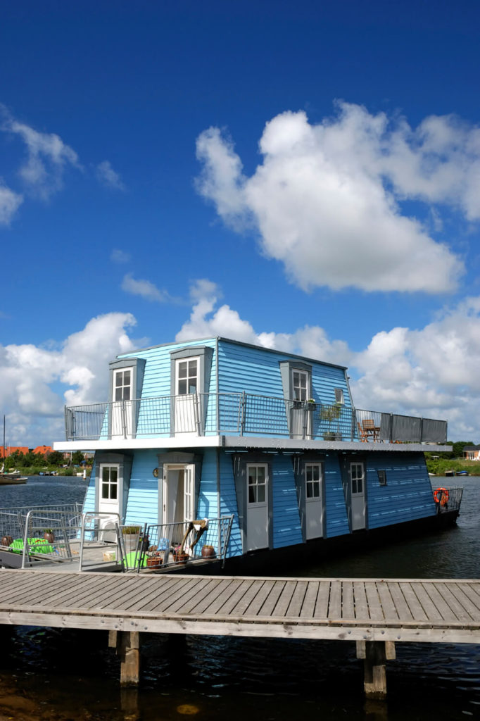 A baby blue two-story trapezoidal houseboat with a large variety of decks and balconies, perfect for the owners to sit and enjoy the breeze. A baby blue two-story trapezoidal houseboat with a large variety of decks and balconies, perfect for the owners to sit and enjoy the breeze.