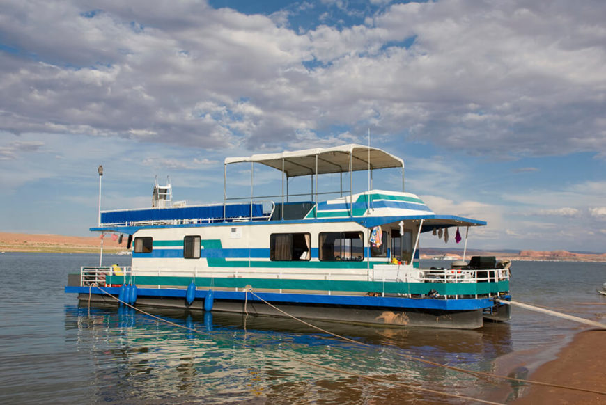 A large houseboat with two covered decks and a large enclosed living area. This boat is large enough to be used for leisure cruises, and is currently moored off of a beach. A large houseboat with two covered decks and a large enclosed living area. This boat is large enough to be used for leisure cruises, and is currently moored off of a beach.
