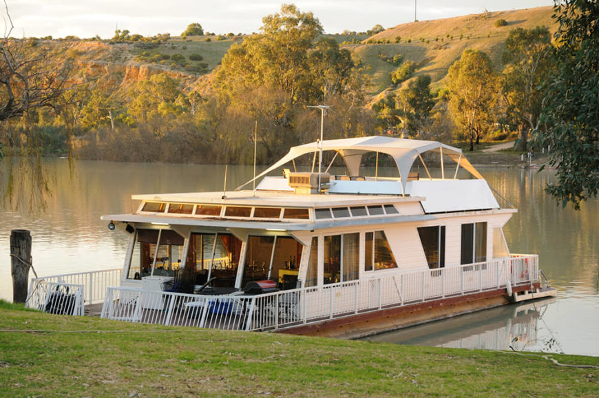 A large luxurious house boat with a covered deck at the top and a large seating area on either side of the boat. The inside is dotted with windows so the owners can enjoy the view. A large luxurious house boat with a covered deck at the top and a large seating area on either side of the boat. The inside is dotted with windows so the owners can enjoy the view.