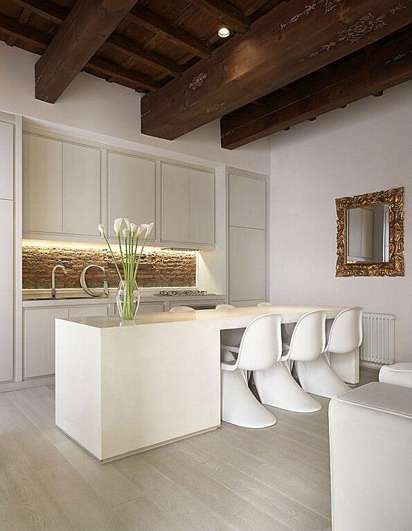White and pale gray create this space, broken up only by accents of gold and green; until you get to the dark, exposed beams on the ceiling of the room. The kitchen itself flourishes with the addition of the rough stone backsplash bringing in color, though neutral, that stands out against the light hues of the rest of the room. White and pale gray create this space, broken up only by accents of gold and green; until you get to the dark, exposed beams on the ceiling of the room. The kitchen itself flourishes with the addition of the rough stone backsplash bringing in color, though neutral, that stands out against the light hues of the rest of the room.