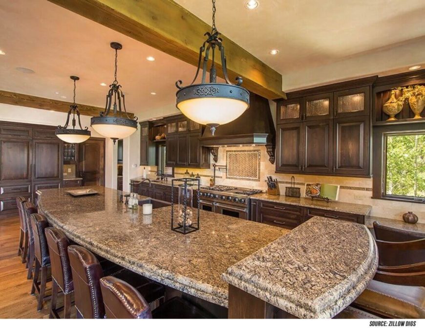 The leather chairs added to this room match the shade of the lower cabinets in the stately kitchen design. Light countertops match the colors of the tile backsplash and offsets the dark wood of the cabinetry. Large pendant lights add a soft glow to the room. The leather chairs added to this room match the shade of the lower cabinets in the stately kitchen design. Light countertops match the colors of the tile backsplash and offsets the dark wood of the cabinetry. Large pendant lights add a soft glow to the room.