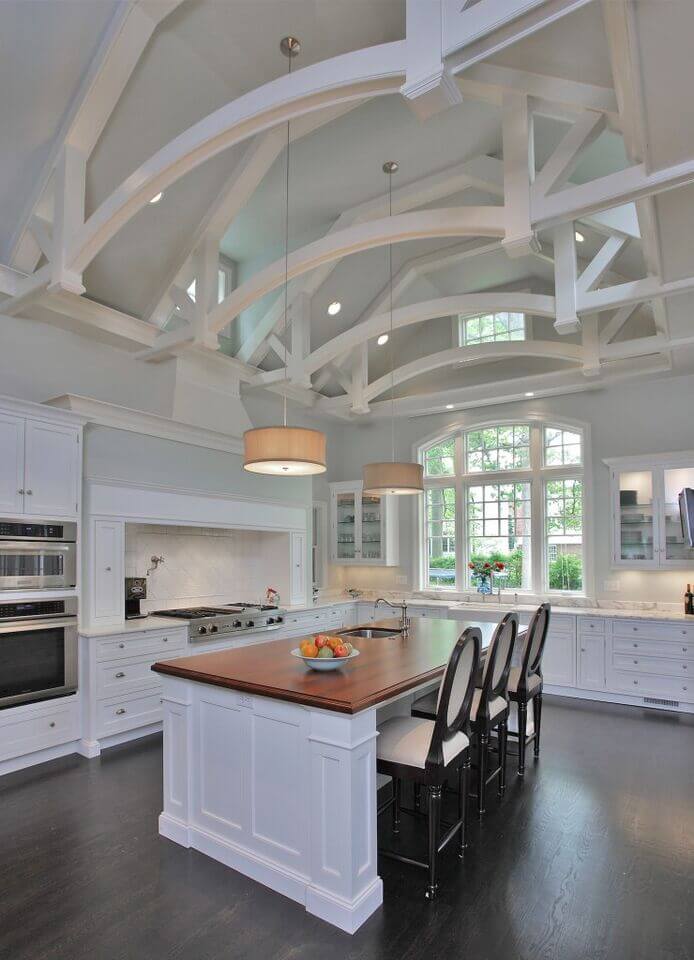 Soaring ceilings are broken up by beautiful arching beams in this stunning white kitchen. Dark floors counter the lightness of the room with the help of the barstools. A gorgeous wood countertop breaks up the space and adds another level of color to the room. Soaring ceilings are broken up by beautiful arching beams in this stunning white kitchen. Dark floors counter the lightness of the room with the help of the barstools. A gorgeous wood countertop breaks up the space and adds another level of color to the room.