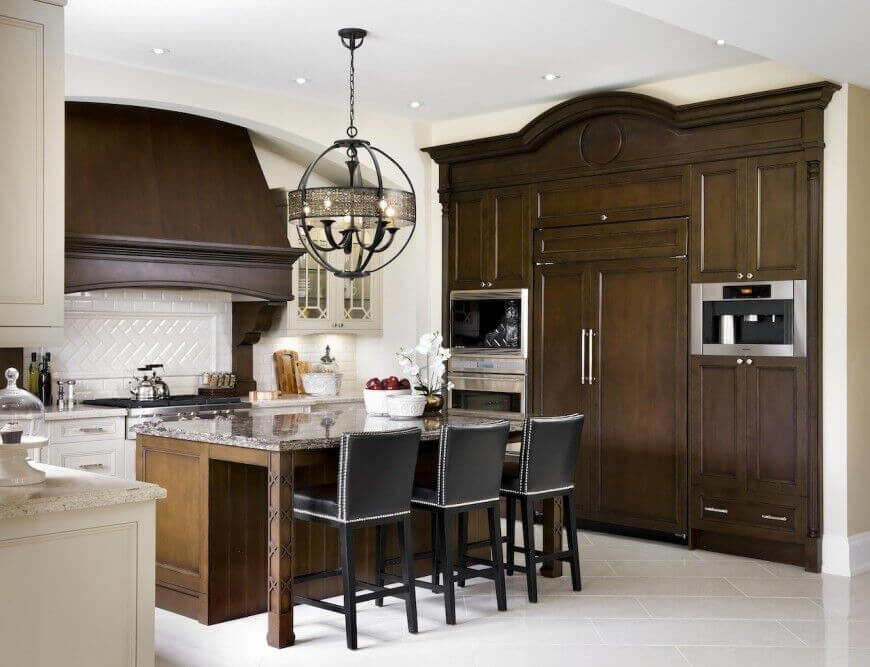 Bold, dark wood is the staple piece of this room, with a dash of white to show off the lovely finish of the wood. Silver and black accents liven up the room and the chandelier over the island is a sight to behold. Bold, dark wood is the staple piece of this room, with a dash of white to show off the lovely finish of the wood. Silver and black accents liven up the room and the chandelier over the island is a sight to behold.