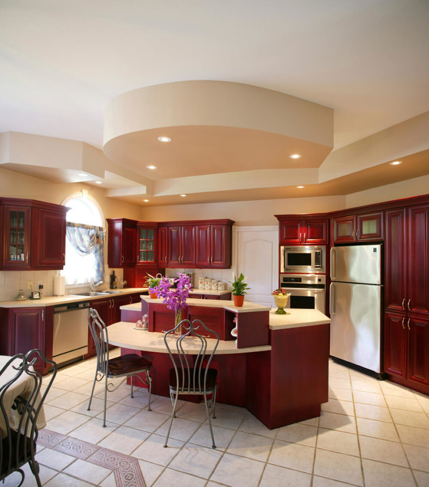 Bold red cabinetry is balanced by creamy counters and floors. The chairs highlight the stainless steel of the appliances with their simple silver frames. Little splashes of color are introduced into the room through plants and flowers - which help to liven up the space. Bold red cabinetry is balanced by creamy counters and floors. The chairs highlight the stainless steel of the appliances with their simple silver frames. Little splashes of color are introduced into the room through plants and flowers - which help to liven up the space.