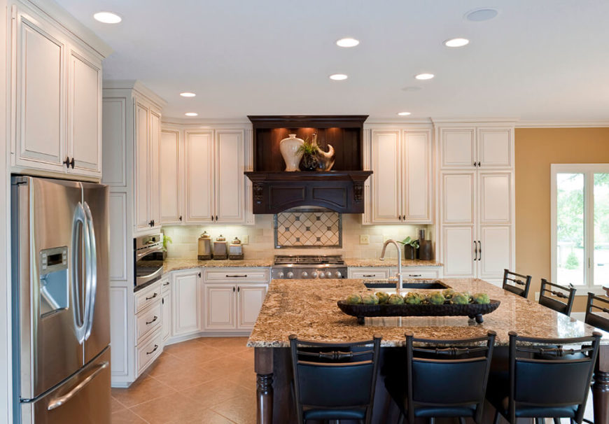 Dark wood successfully breaks up the use of white cabinetry against the tan backdrop created by the floor and walls. Dark chairs continue to ground the space and pops of bright green bring bits of color and life, carrying the eyes around the rest of the room. Dark wood successfully breaks up the use of white cabinetry against the tan backdrop created by the floor and walls. Dark chairs continue to ground the space and pops of bright green bring bits of color and life, carrying the eyes around the rest of the room.