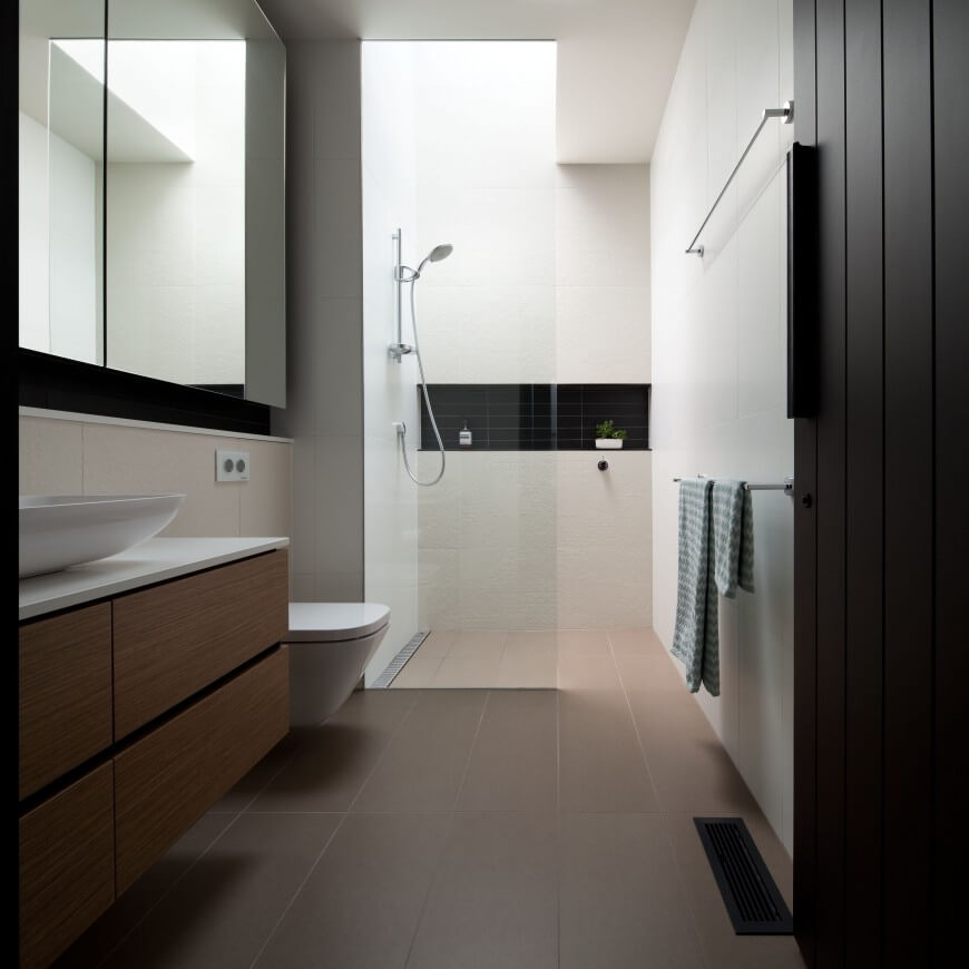 Primary bathroom features a wooden floating vanity topped with white marble and a vessel sink. It has a walk-in shower accented with a black subway tile backsplash.