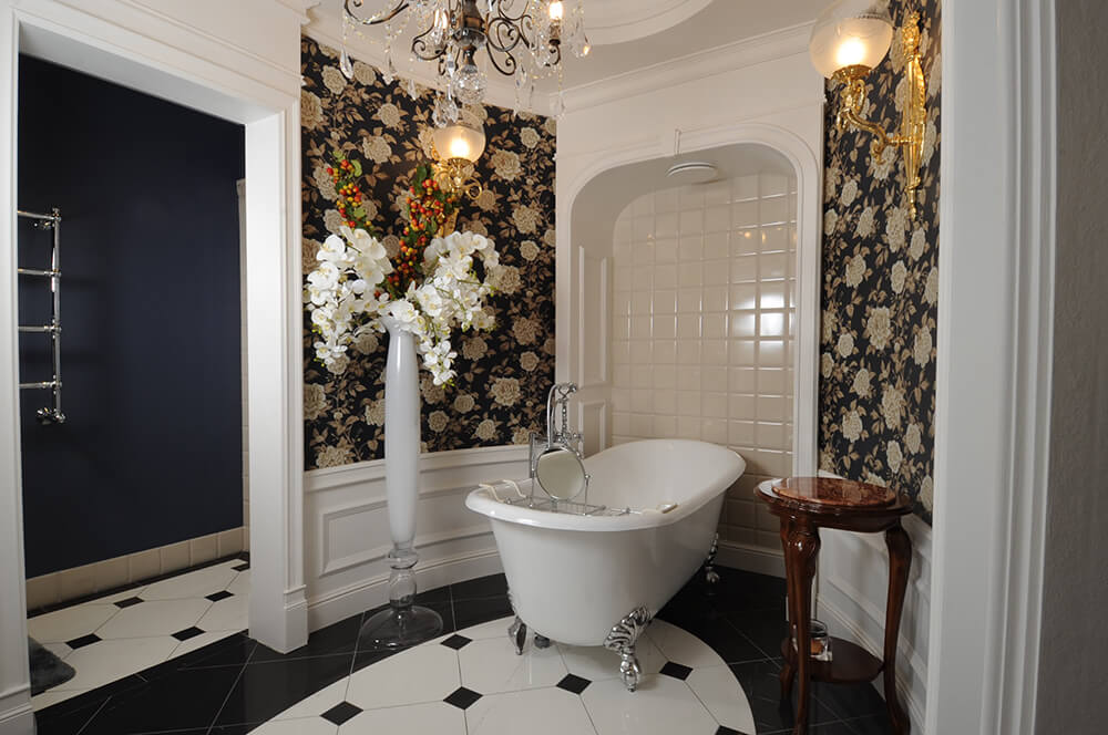 This bathroom boasts elegant walls and indoor flowers in vase lighted by wall lighting. The tiles flooring looks classy as well.