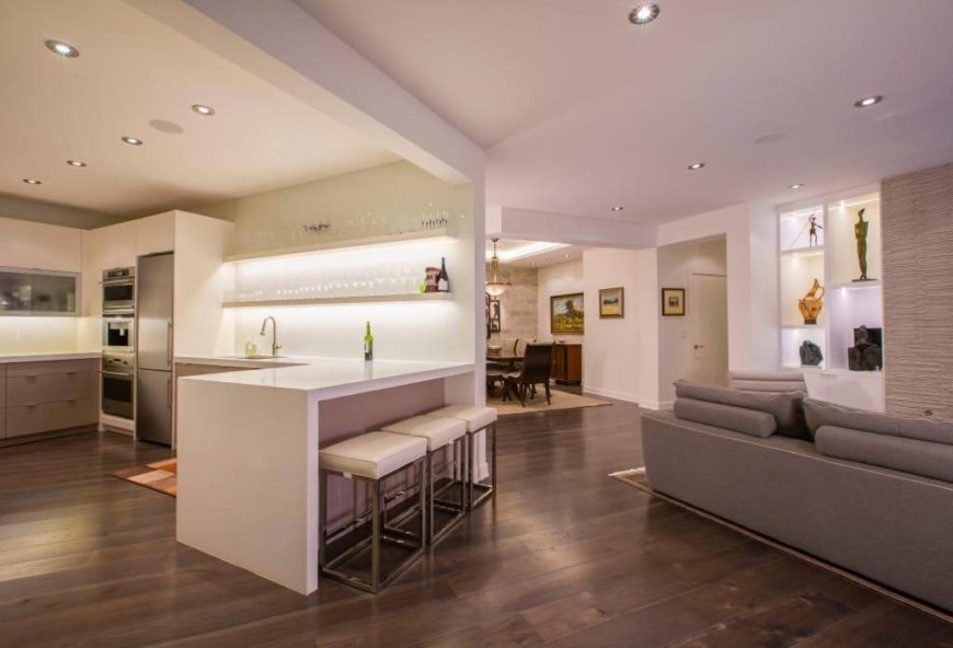 White kitchen with stainless steel appliances and smooth counters with hardwood floors and recessed lights.