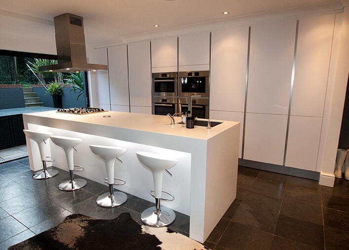 Large single wall kitchen with white cabinetry and smart appliances along with large center island lighted by recessed ceiling lights.