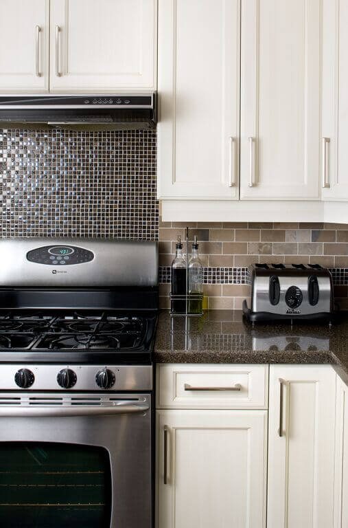 Kitchen showcasing white cabinetry, tiles backsplash, smart appliances and solid countertop.