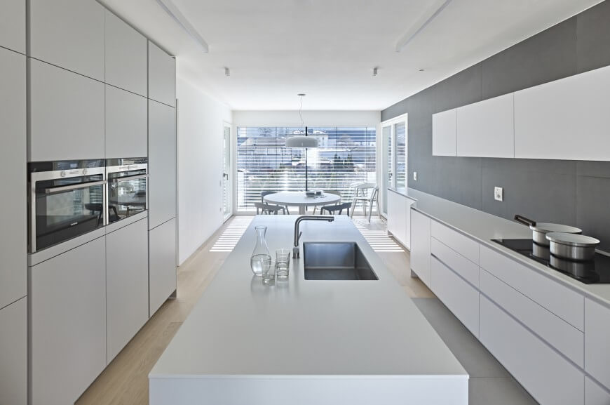 Galley type kitchen with smooth white countertops and cabinetry along with a large center island and smart appliances.