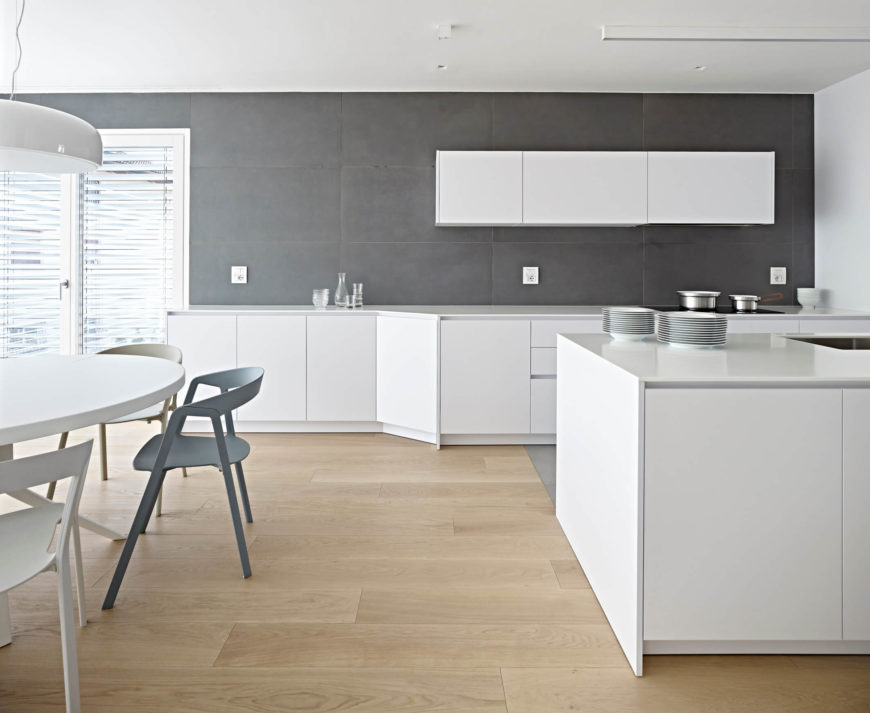 Kitchen with a large gray tiles backsplash and smooth white cabinetry and countertops along with a dine-in round table set.