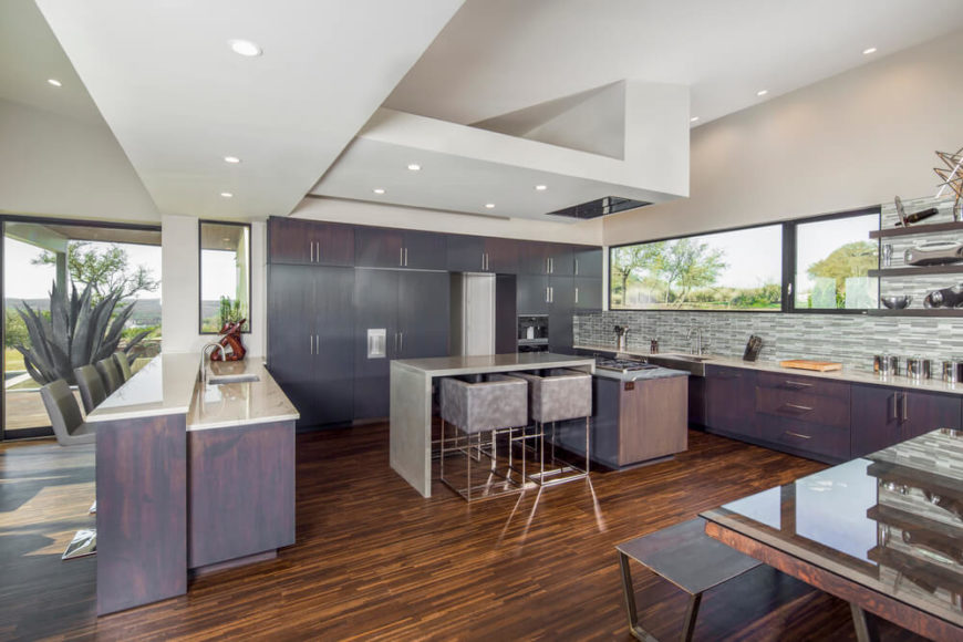 Large kitchen with stylish wooden cabinetry and marble countertops along with a breakfast bar and dine-in table set.