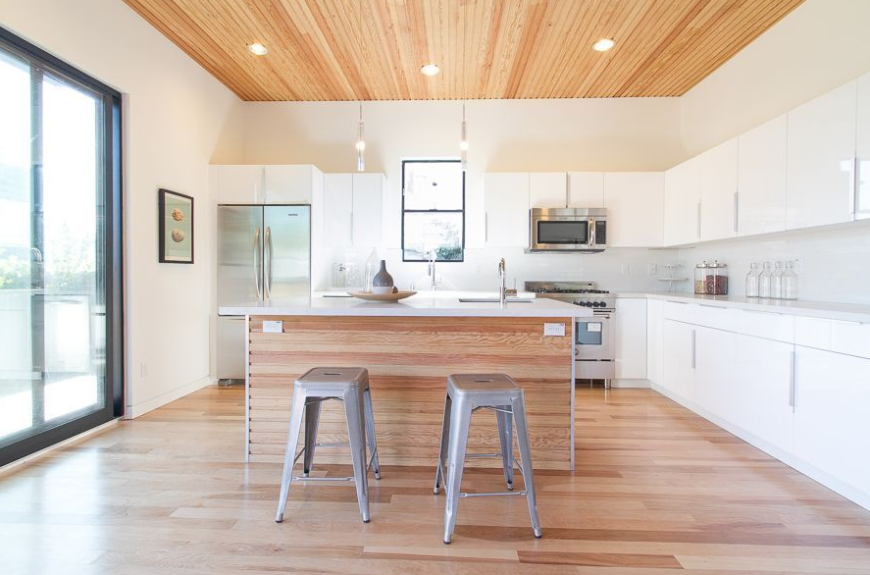 Simple L shape kitchen with white walls and hardwood flooring along with marble countertops and recessed ceiling lights.